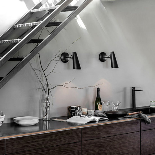 Eine Küche aus dunklem Holz mit mit schwarzen Armaturen und zwei schwarzen Wandleuchten aus Metall, wirkt schlicht und klar.