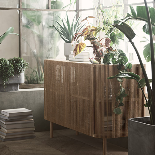 Ein Sideboard mit Fronten aus filigranen Holzstäben und mit abgerundeten Ecken bietet Stellfläche für verschiedene Grünpflanzen 
